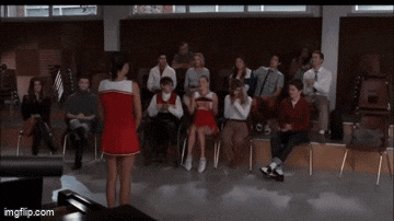 two cheerleaders are dancing in front of a crowd of people in a classroom .