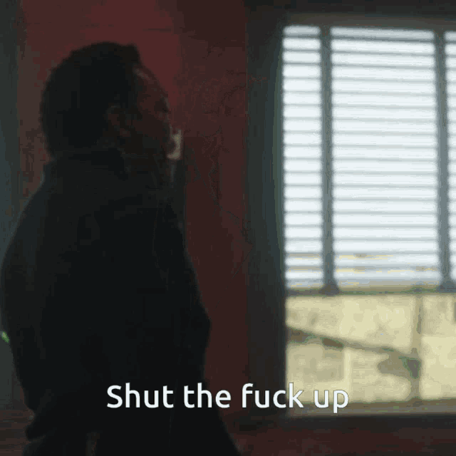 a man standing in front of a window with the words shut the fuck up below him