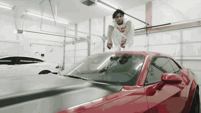 a man sitting on top of a red sports car in a garage