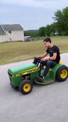 a man is riding a john deere lawn mower down the road