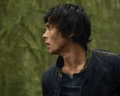 a man with wet hair is standing in the woods and looking at the camera with a surprised look on his face .