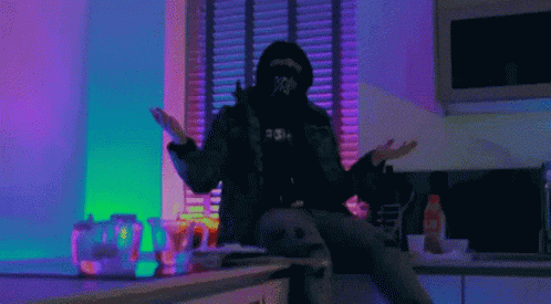 a man wearing a hoodie that says x on it is sitting on a counter in a kitchen