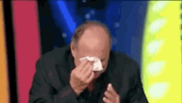 a bald man in a suit and tie is covering his face with a napkin .