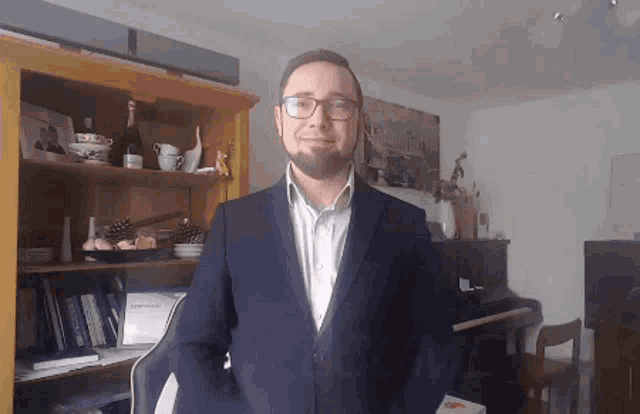 a man in a suit stands in front of a bookshelf