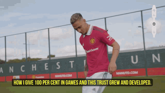 a man in a pink teamviewer jersey stands in front of a manchester united sign
