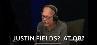 a man wearing headphones is sitting in front of a microphone and saying justin fields ? at qb ?