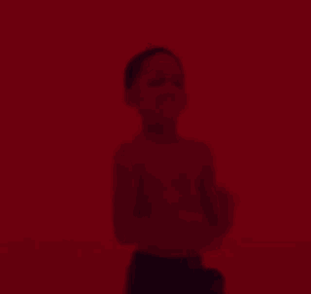 a shirtless child is standing in front of a red wall .