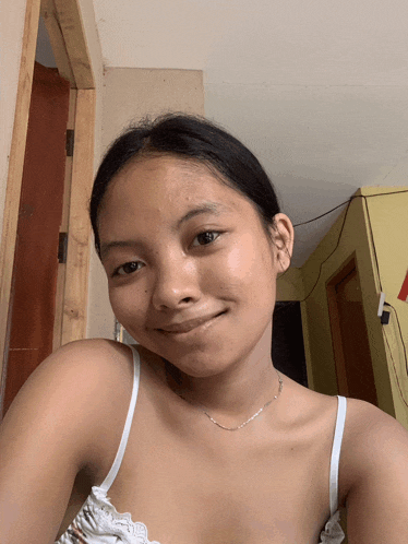 a young girl wearing a white tank top and a silver chain smiles for the camera