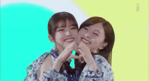 two asian girls are making a heart shape with their hands .