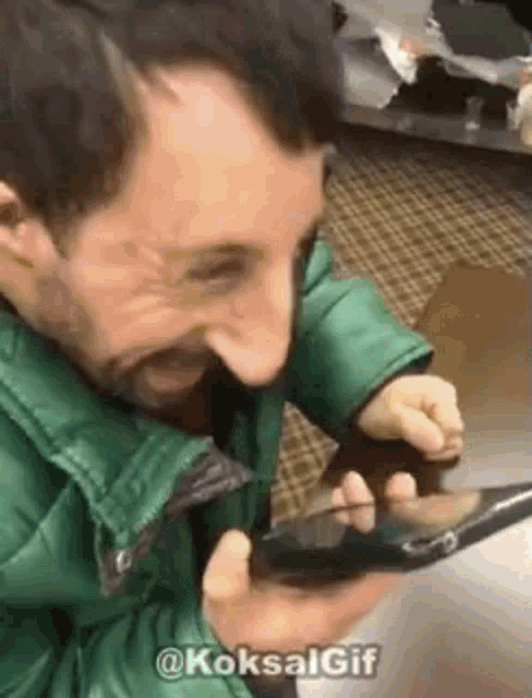 a man in a green jacket is holding a cell phone in his hands .