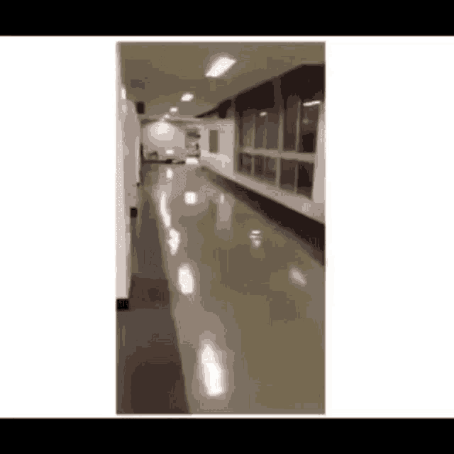 a long hallway in a building with a lot of windows and a shiny floor .