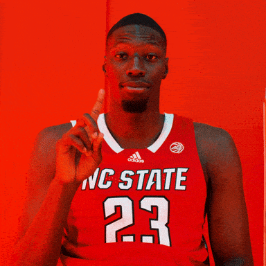 a man in a red nc state jersey points up