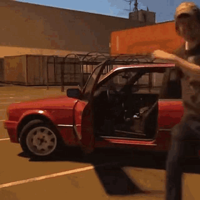 a man is standing next to a red car in a parking lot