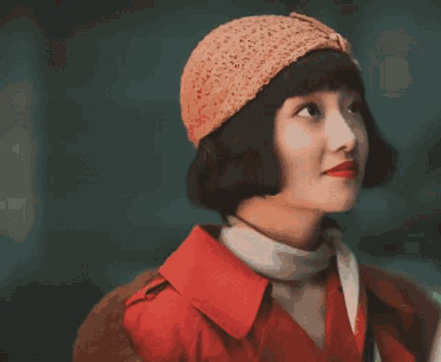 a woman wearing a hat and a red coat looks up
