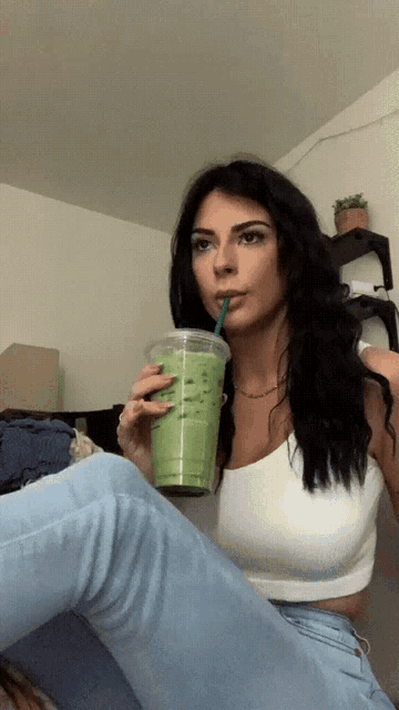 a woman drinking a green smoothie from a plastic cup