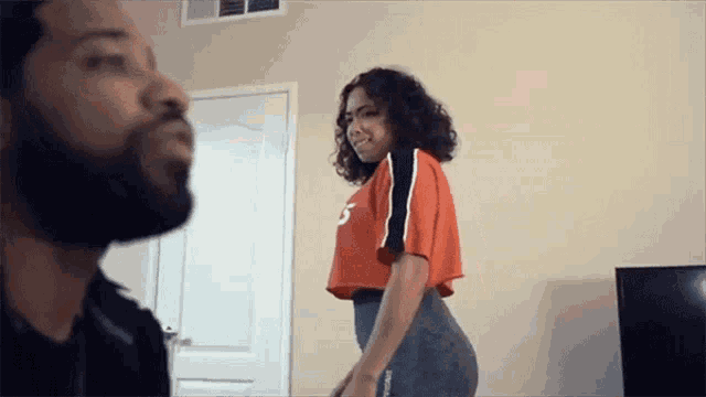 a woman in a crop top with the number 5 on it is standing next to a man