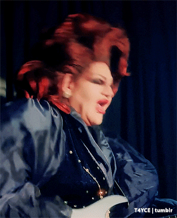 a drag queen with red hair is wearing a blue shirt and earrings