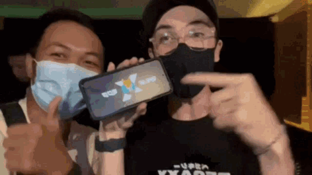 two men wearing masks are holding up a cell phone that says super x on it