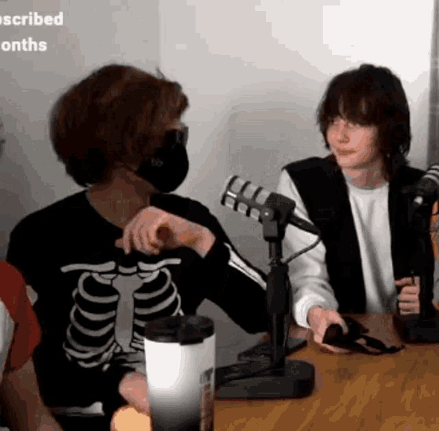 a man wearing a skeleton shirt is sitting at a table with a microphone in front of him .