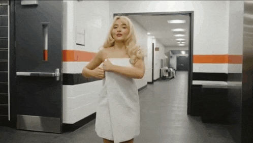 a woman is wrapped in a white towel and standing in a hallway .