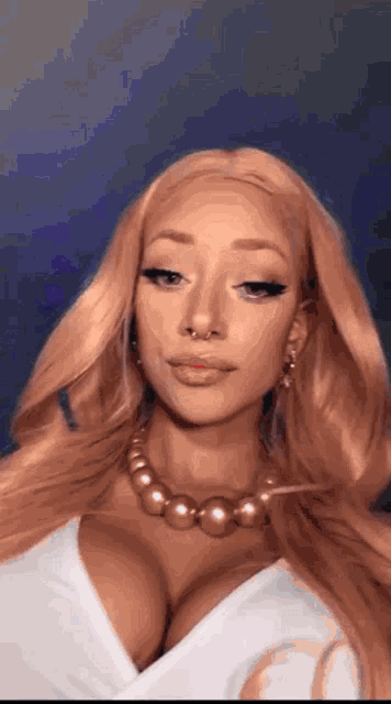 a woman with long blonde hair and a nose ring is wearing a pearl necklace and earrings .