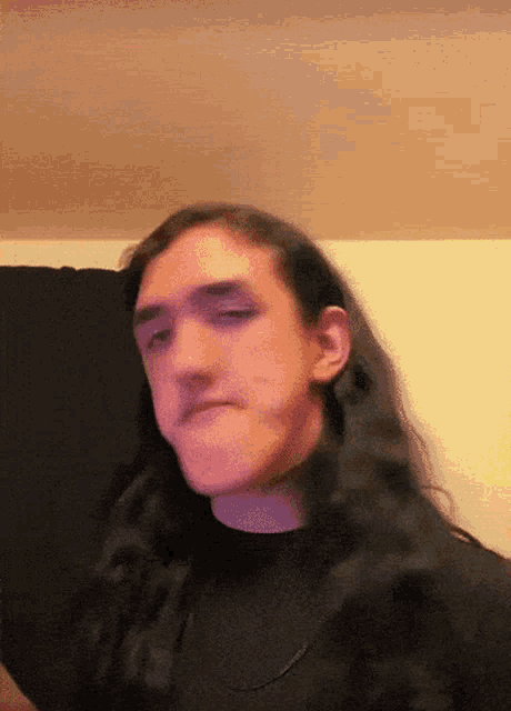 a man with long hair is wearing a black shirt and a necklace