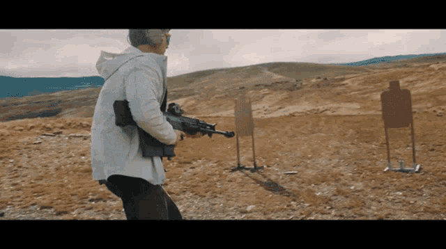 a man in a white jacket is holding a rifle in a field
