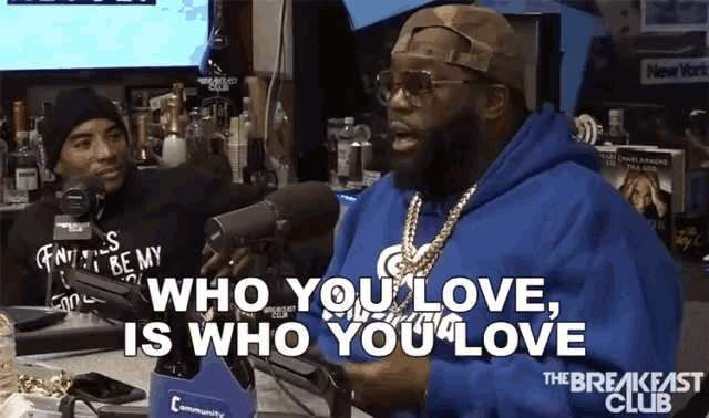 a man speaking into a microphone with the words who you love is who you love behind him