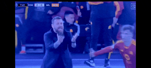 a man with a beard is standing in front of a soccer player on a field .