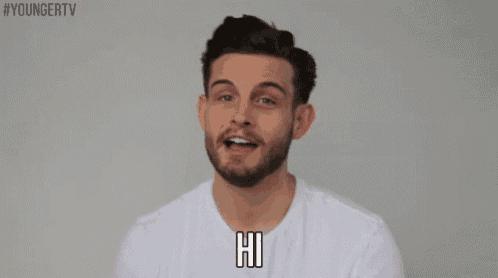 a man with a beard wearing a white shirt is smiling and saying hi .