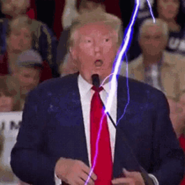 a man in a suit and tie is speaking into a microphone while a lightning bolt is coming out of his mouth .
