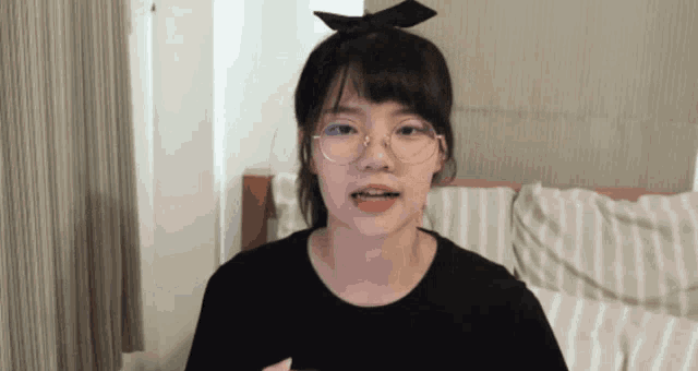 a girl wearing glasses and a bow in her hair looks at the camera