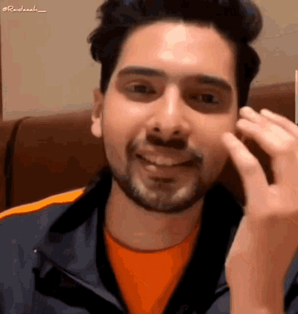 a man with a beard wearing an orange shirt and a blue jacket
