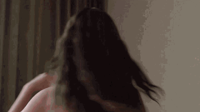 a woman with long hair is standing in front of a curtain .