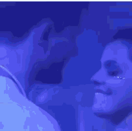 a man and woman are kissing in a dark room with blue lights .
