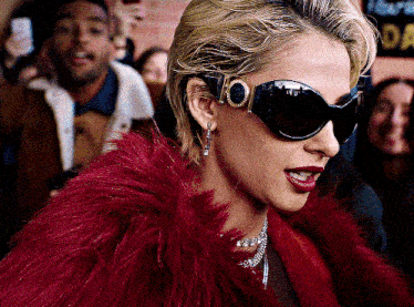 a woman wearing sunglasses and a red fur coat has the number 101 on her glasses