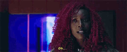 a woman with purple curly hair is talking in a room .
