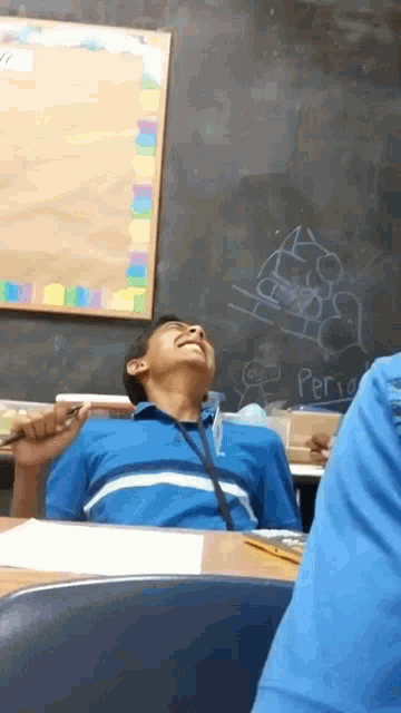 a boy laughs in front of a blackboard that says period