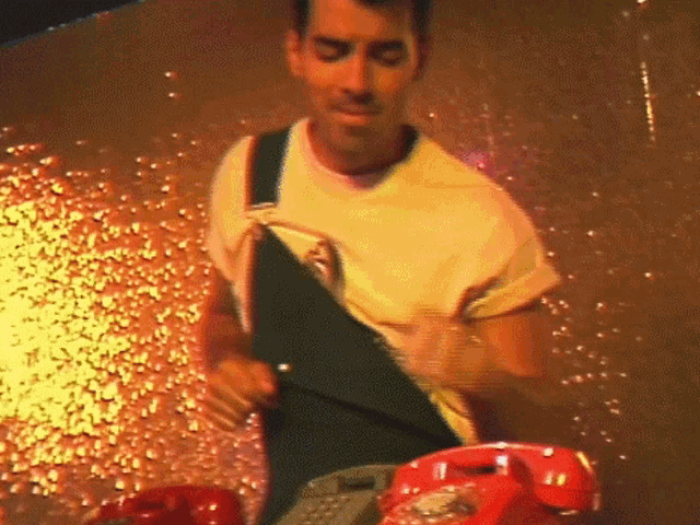 a man in a yellow shirt is standing next to a red phone .