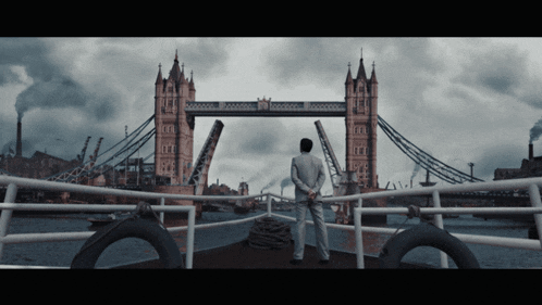 a man in a suit stands on a boat looking at the tower bridge