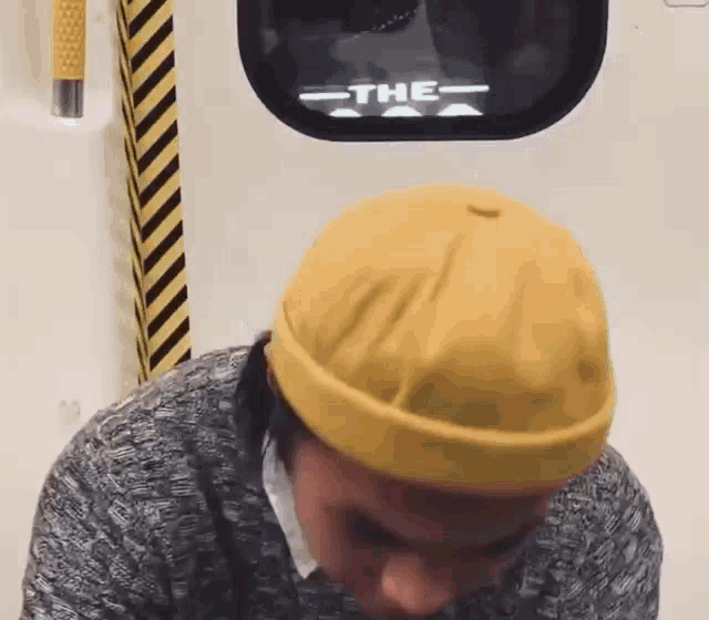 a man wearing a yellow hat is sitting in front of a window that says " the "