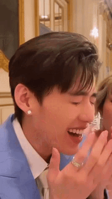 a man in a blue suit and white shirt is laughing while holding his hand to his mouth .