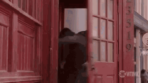 a man is coming out of a red phone booth .