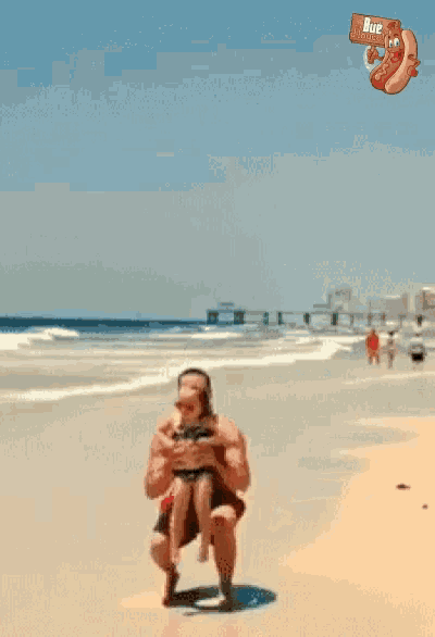 a man is carrying a woman in his arms on a beach with a hot dog in the background