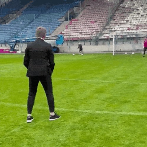 a man in a suit stands on a soccer field in front of an empty stadium