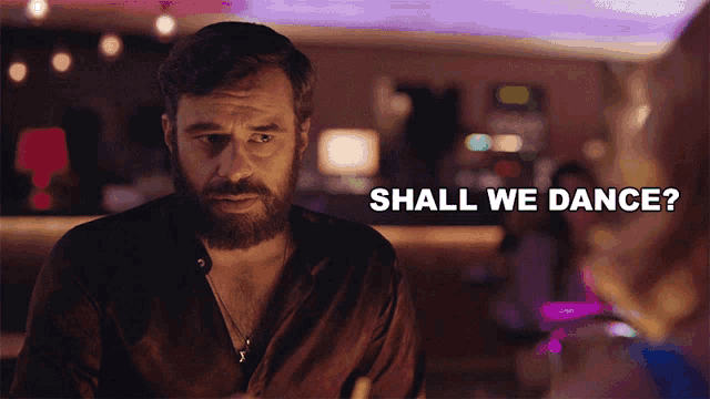 a man with a beard says shall we dance in a bar