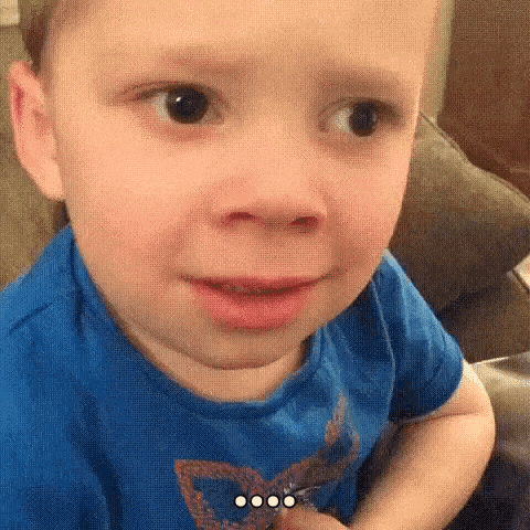 a little boy in a blue shirt is making a funny face .