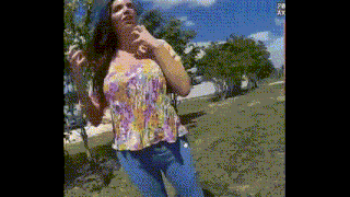 a woman is standing in a park wearing a floral shirt and jeans .