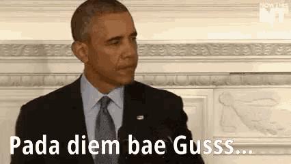 barack obama is standing in front of a microphone in a suit and tie and talking .