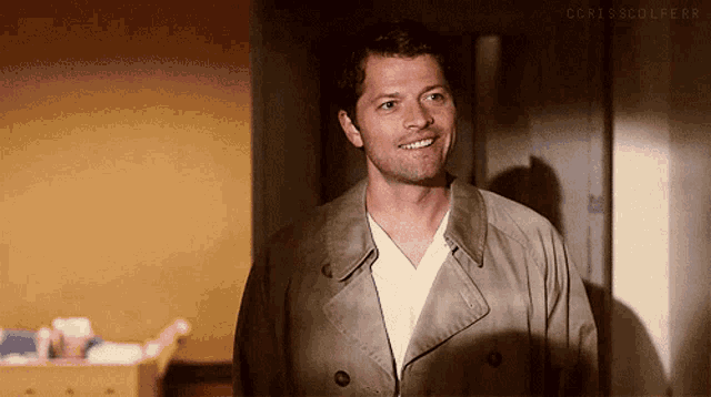 a man in a trench coat and white shirt is smiling in a room .